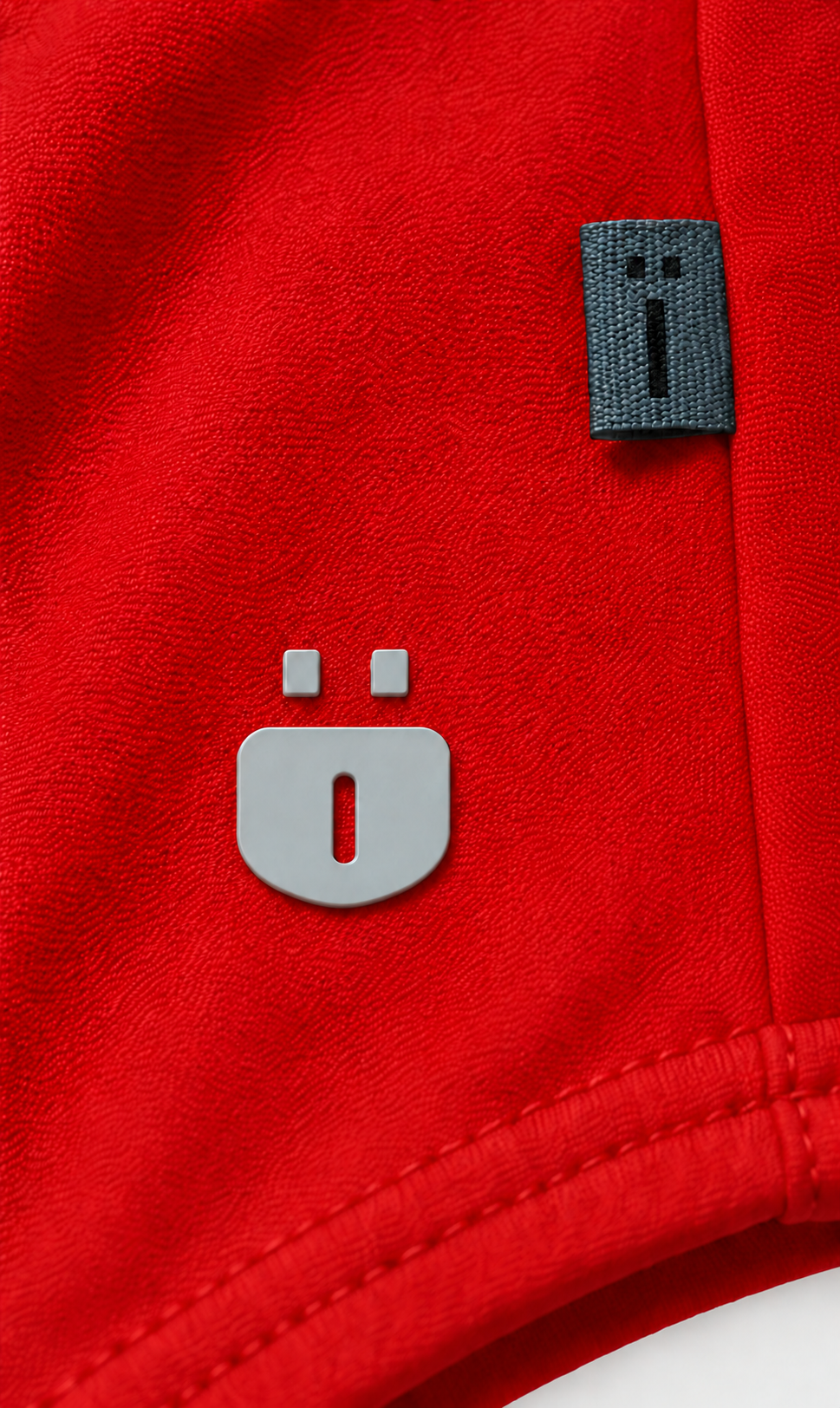 Close-up of a bright red textured garment, likely a sweatshirt or jacket, featuring a large gray stylized 'O' logo on the front and a small dark gray fabric brand tag near the upper right.